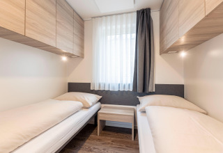 Moderne soveværelse med to enkeltsenge, lyse træskabe og stort vindue i Chalets & Glamping Nassfeld 2, Østrig.