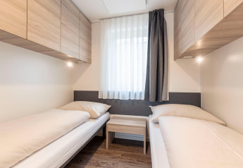 Camera moderna con due letti singoli, armadi in legno e grande finestra presso Chalets & Glamping Nassfeld 2, Austria.