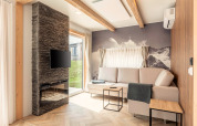 Helles Wohnzimmer im Chalets & Glamping Nassfeld 3 in Österreich mit Sofa, Kamin, TV und Bergmotiv.