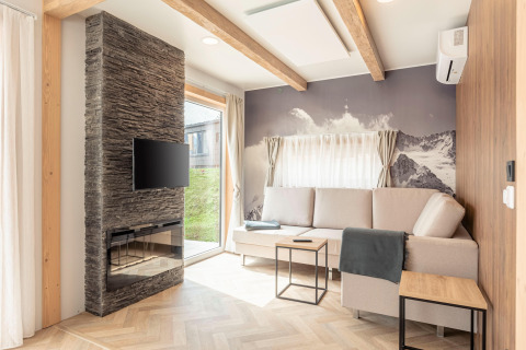 Lichte woonkamer bij Chalets & Glamping Nassfeld 3 in Oostenrijk met bank, haard, tv en bergmuurschildering.