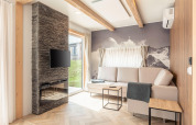 Soggiorno luminoso ai Chalets & Glamping Nassfeld 3 in Austria con divano, camino, TV e murale di montagna.