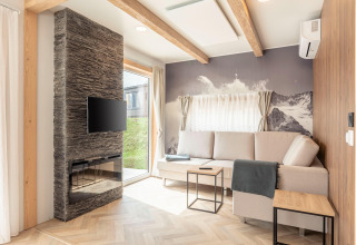 Lichte woonkamer bij Chalets & Glamping Nassfeld 3 in Oostenrijk met bank, haard, tv en bergmuurschildering.