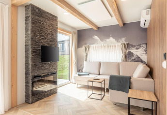 Soggiorno luminoso ai Chalets & Glamping Nassfeld 3 in Austria con divano, camino, TV e murale di montagna.