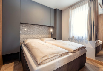 Modernes Schlafzimmer mit Doppelbett, grauen Schränken und großem Fenster im Chalets «& Glamping Nassfeld 3» in Österreich.