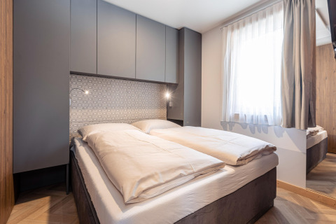 Moderne slaapkamer met tweepersoonsbed, grijze kasten, patroonmuur en groot raam bij Chalets «& Glamping Nassfeld 3» in Oostenrijk.