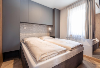 Moderne slaapkamer met tweepersoonsbed, grijze kasten, patroonmuur en groot raam bij Chalets «& Glamping Nassfeld 3» in Oostenrijk.