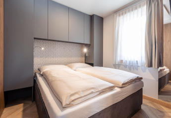 Camera da letto moderna con letto matrimoniale, armadi grigi, parete decorata e grande finestra al Chalets «& Glamping Nassfeld 3» in Austria.