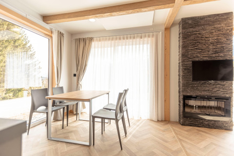 Moderne eetkamer in een chalet bij Nassfeld met grote ramen, stenen haard, tafel en vier stoelen.
