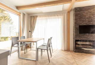 Moderne eetkamer in een chalet bij Nassfeld met grote ramen, stenen haard, tafel en vier stoelen.
