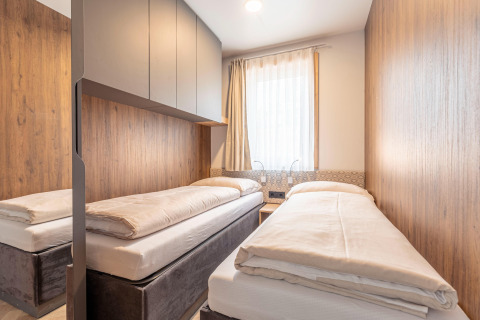 Sfeervolle slaapkamer met twee eenpersoonsbedden, houten panelen en opbergruimte in Chalets & Glamping Nassfeld 3, Oostenrijk.