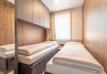 Camera accogliente con due letti singoli, pannelli in legno e armadi al Chalets & Glamping Nassfeld 3, Austria.
