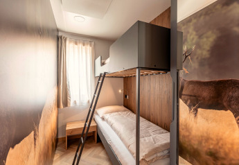 Modernes Zimmer mit Etagenbett, Naturbild von einem Hirsch, Holztisch und Fenster im Chalets & Glamping Nassfeld 3.