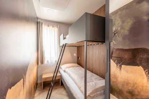 Moderne kamer met stapelbed, hertenmuurschildering, houten tafeltje en raam bij Chalets & Glamping Nassfeld 3.
