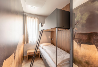 Moderne kamer met stapelbed, hertenmuurschildering, houten tafeltje en raam bij Chalets & Glamping Nassfeld 3.