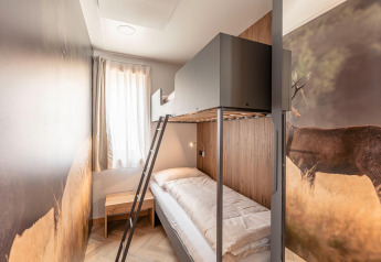 Camera moderna con letto a castello, murale di cervo, tavolino di legno e finestra al Chalets & Glamping Nassfeld 3.