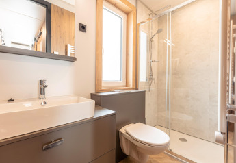 Bagno moderno con WC sospeso, doccia in vetro, lavabo e finestra presso Chalets & Glamping Nassfeld 3 in Austria.