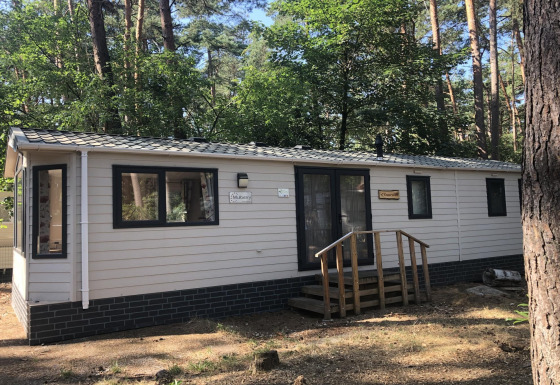 Et billede af et chalet kaldet Koperwiek, omgivet af træer i et skovområde på en solrig dag.