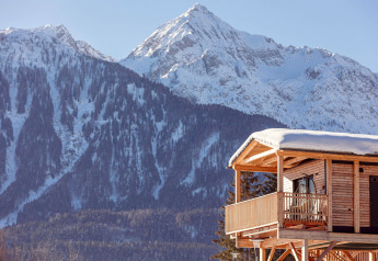 Ein Holzchalet mit Balkon und Schneedecke im Vordergrund, vor verschneiten Bergen in Österreich.