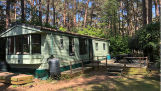 Casa móvil en Sijs Lodge rodeada de bosque, con terraza de madera y zona de estar al aire libre.