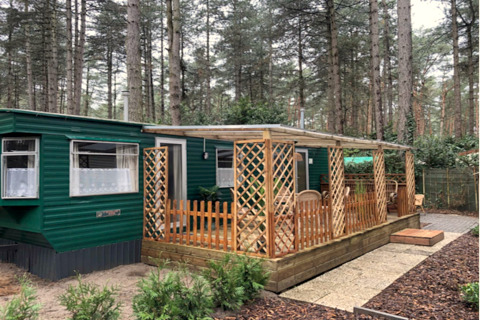 Chalet Specht in het woud met groene buitenkant, groot raam en overdekt terras met houten meubilair.