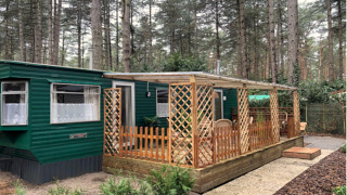 Chalet Specht au cœur de la forêt, façade verte, grande fenêtre et terrasse couverte avec meubles en bois.