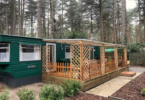 Chalet Specht au cœur de la forêt, façade verte, grande fenêtre et terrasse couverte avec meubles en bois.