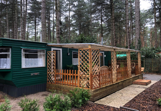 Chalet Specht au cœur de la forêt, façade verte, grande fenêtre et terrasse couverte avec meubles en bois.
