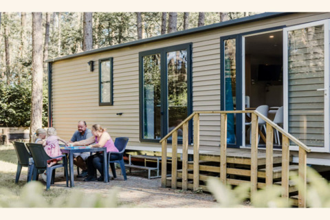Een gezin zit buiten aan een tafel voor de Sparrowhawk lodge, omgeven door bomen en natuur.