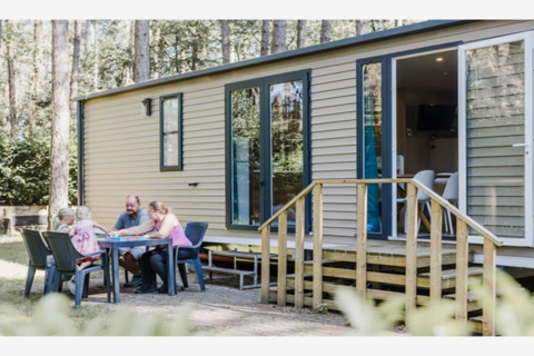 Une famille est assise à l'extérieur à une table devant le lodge Sparrowhawk, entourée d’arbres et de nature.