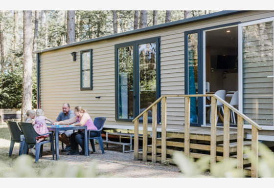 Une famille est assise à l'extérieur à une table devant le lodge Sparrowhawk, entourée d’arbres et de nature.