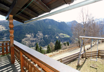 Blick von Balkon des Chalet Pirkach in Österreich mit Alpenpanorama, Wäldern und Schaukeln im Garten.