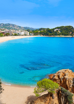Prachtige baai bij een vakantiepark met glamping, goud zandstrand, helderblauw water en groene omgeving.