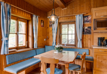 Gemütliche Essecke im Chalet «Pirkach» in Österreich mit Holzverkleidung, blauen Vorhängen und Sitzbank.