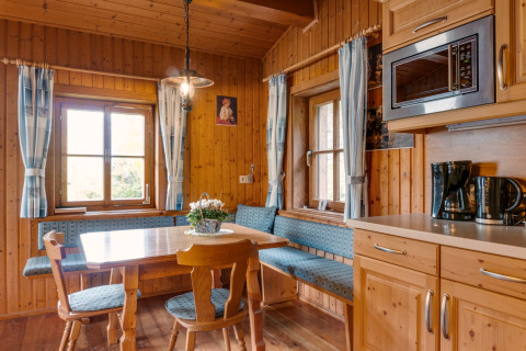 Hyggeligt træbeklædt spisestue og køkken i Chalet Pirkach, Østrig, med blå polstrede bænke og gardiner.