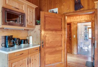 Holzverkleidete Küche im Chalet «Pirkach» in Österreich mit Blick auf das Badezimmer und Geräte.