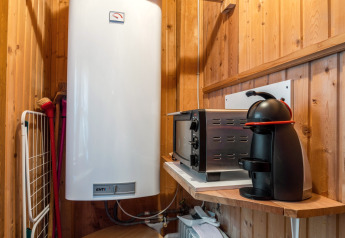 Warmwasserboiler, Ofen und Kaffeemaschine auf Holzregal in Chalet «Pirkach» in Österreich.