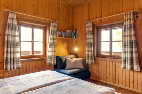 Hygge hjørne med træpaneler, to vinduer, sofakrog, bøger og gardiner i et østrigsk chaletværelse.