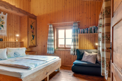 Soveværelse i Chalet Pirkach i Østrig med trævægge, seng, vindue og hyggelig læsehjørne