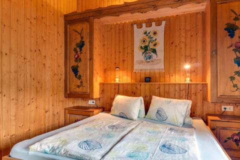 Soveværelse i Chalet «Pirkach» i Østrig med træpaneler, dekorerede skabe og dobbeltseng.