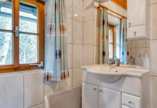 Lyst badeværelse med trævindue, hvide fliser og moderne vask på Chalet «Pirkach» i Østrig.