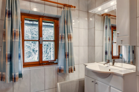 Badeværelse i Chalet «Pirkach» i Østrig med trævindue, fliser, spejl og gardiner med mønster.