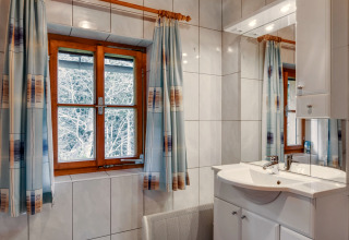 Badeværelse i Chalet «Pirkach» i Østrig med trævindue, fliser, spejl og gardiner med mønster.