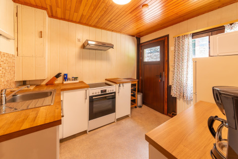 Warme houten keuken in lodge 'Les Bouleaux' in België, met moderne witgoedapparaten en raam.