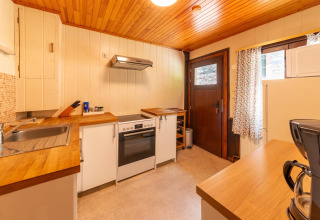 Warme houten keuken in lodge 'Les Bouleaux' in België, met moderne witgoedapparaten en raam.