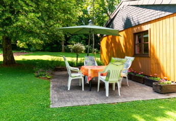 Outdoor patio at lodge «Les Bouleaux» in Belgium with chairs, table, umbrella, and lush green surroundings.