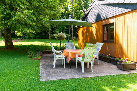 Buitenterras bij lodge «Les Bouleaux» in België met stoelen, tafel, parasol en groene tuinomgeving.