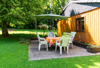 Buitenterras bij lodge «Les Bouleaux» in België met stoelen, tafel, parasol en groene tuinomgeving.
