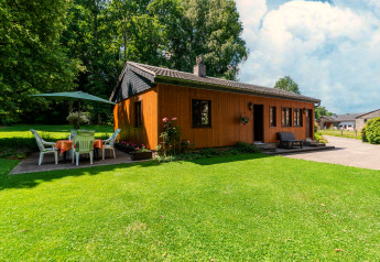 Wooden lodge at Les Bouleaux in Belgium, surrounded by greenery, patio with dining set and large umbrella.