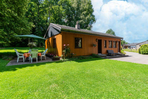 Houten lodge bij Les Bouleaux in België, omgeven door groen, terras met tafel, stoelen en parasol.