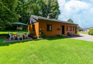 Houten lodge bij Les Bouleaux in België, omgeven door groen, terras met tafel, stoelen en parasol.